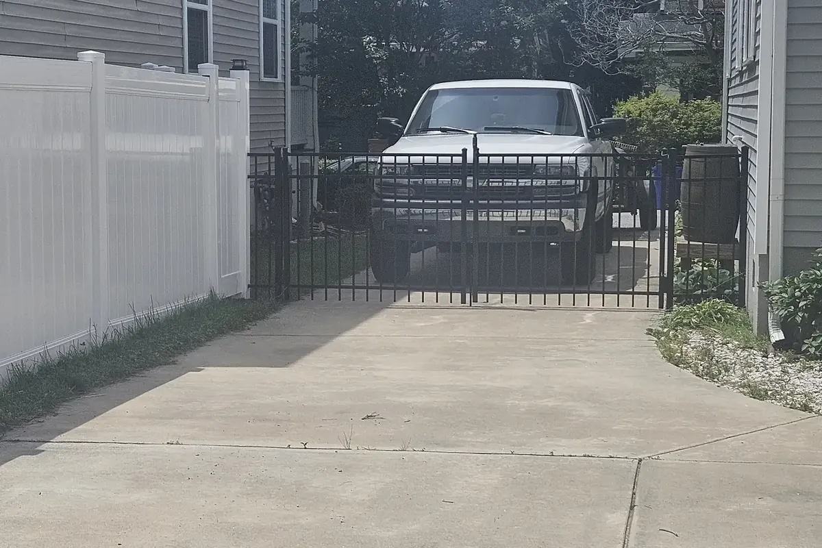 Black aluminum driveway gate beside a white vinyl privacy fence