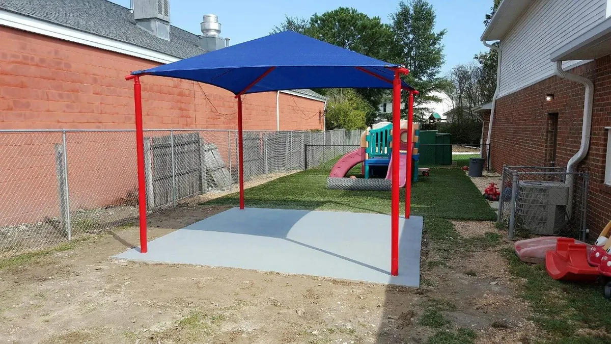 Poured and finished concrete pad under a blue shade canopy beside a chain link fence