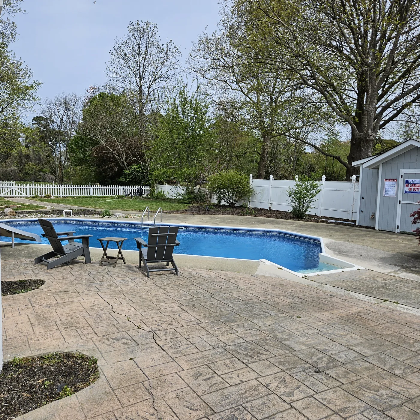 White vinyl privacy fence and picket enclosing a backyard pool and stamped patio