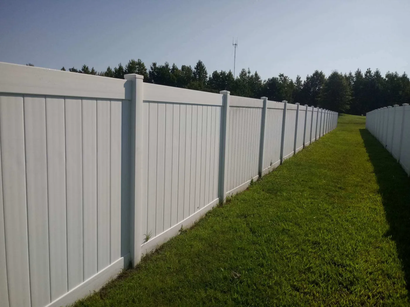 White tongue-and-groove vinyl privacy fence on a long property line