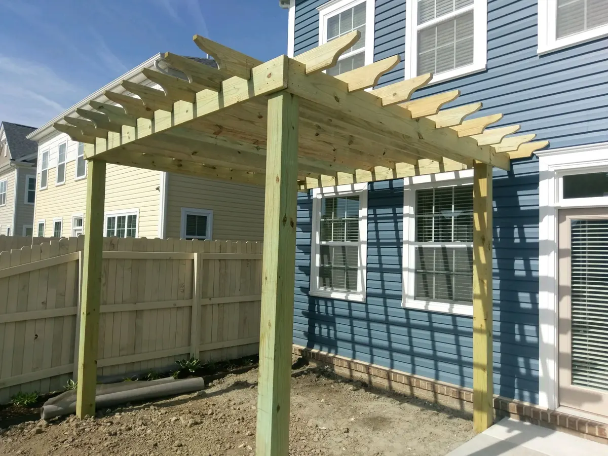 New pressure-treated pergola built against a blue Virginia Beach home beside a wood privacy fence